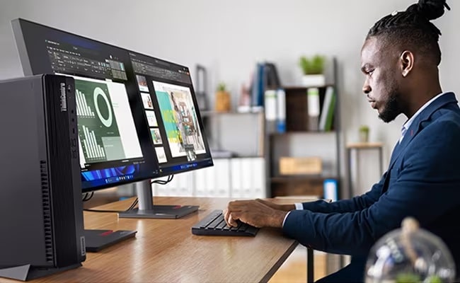 A person at a desk with two Lenovo ThinkVision monitors & the Lenovo ThinkCentre M90s Gen 5 in the foreground.