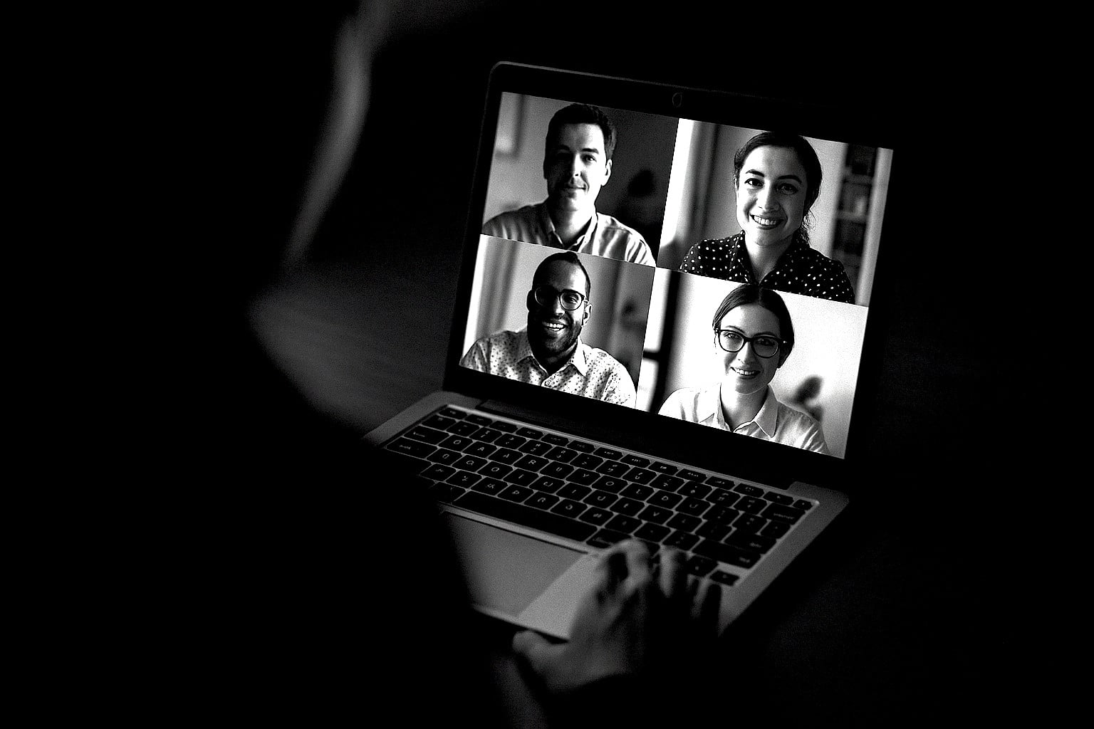 Laptop displaying a video conference with four participants in a 2x2 grid, viewed from behind the user